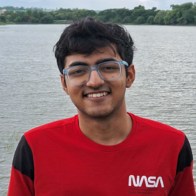 Prakhar Gupta smiling by a lake, wearing glasses and a red NASA t-shirt